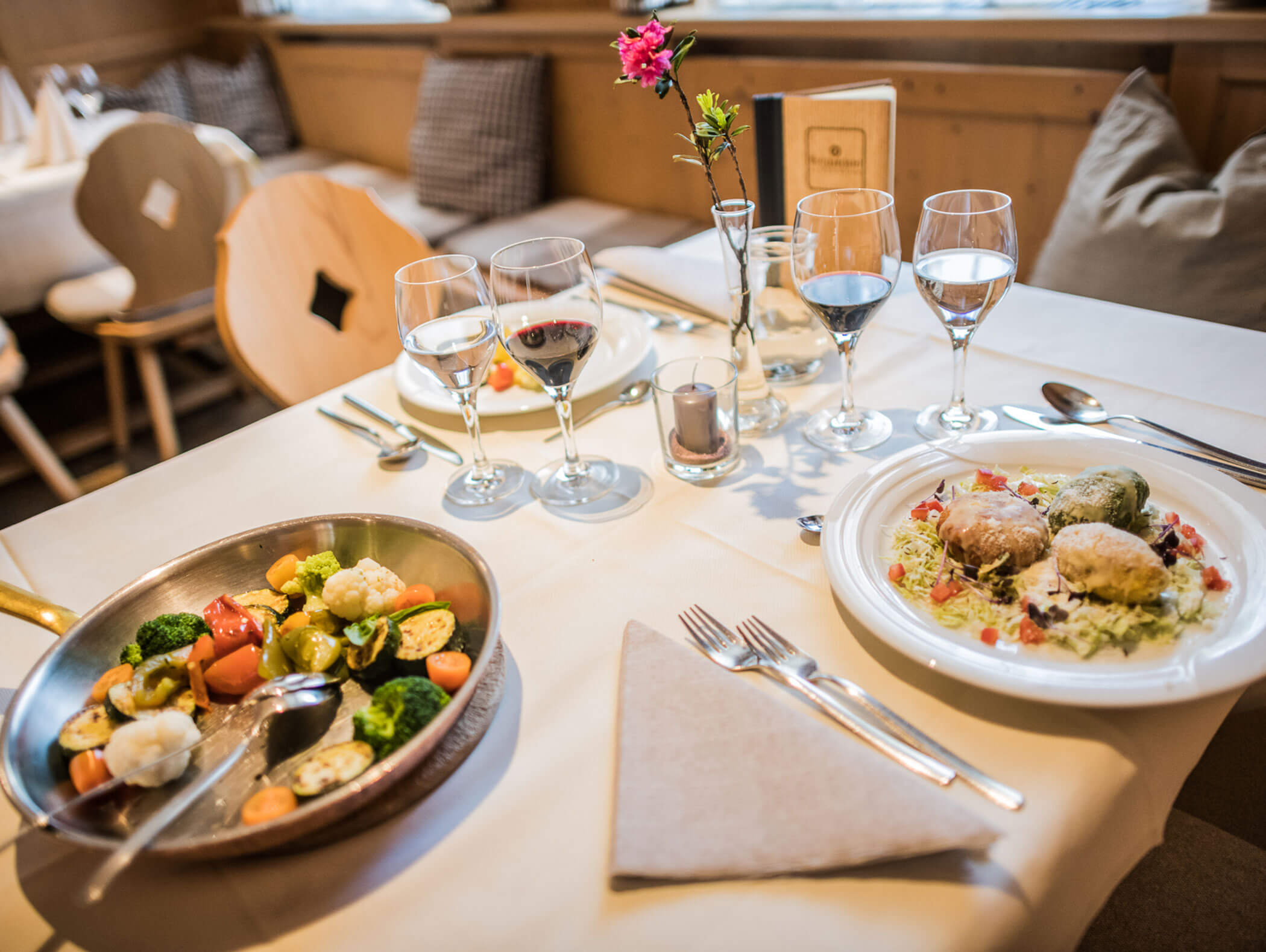Set table with two plates of dumplings, next to a pan of vegetables - Wirtshaushotel Alpenrose