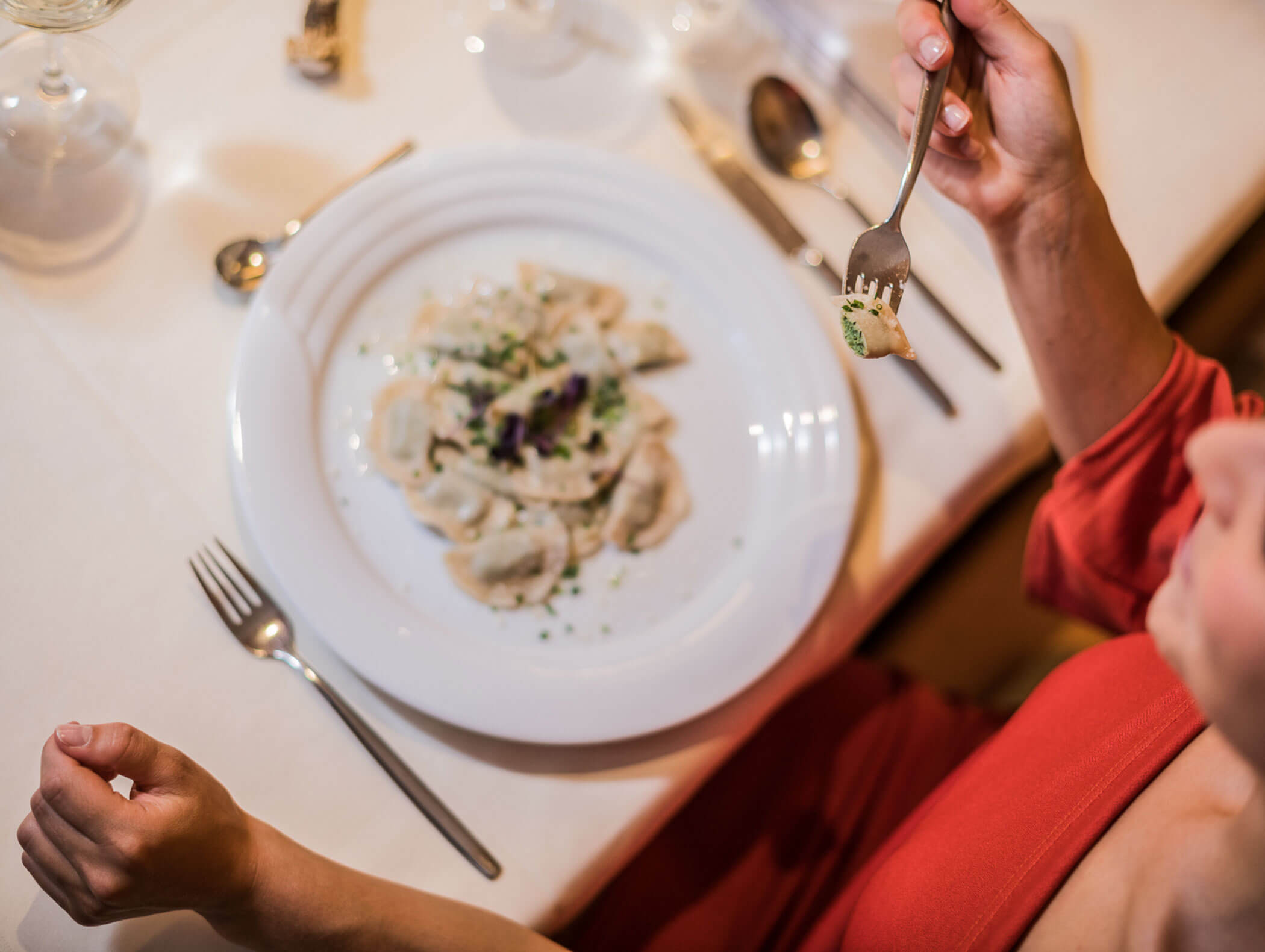 Schlutzkrapfen ravioli on the plate and one hand holding half a Schlutzkrapfen ravioli on the fork - Wirtshaushotel Alpenrose