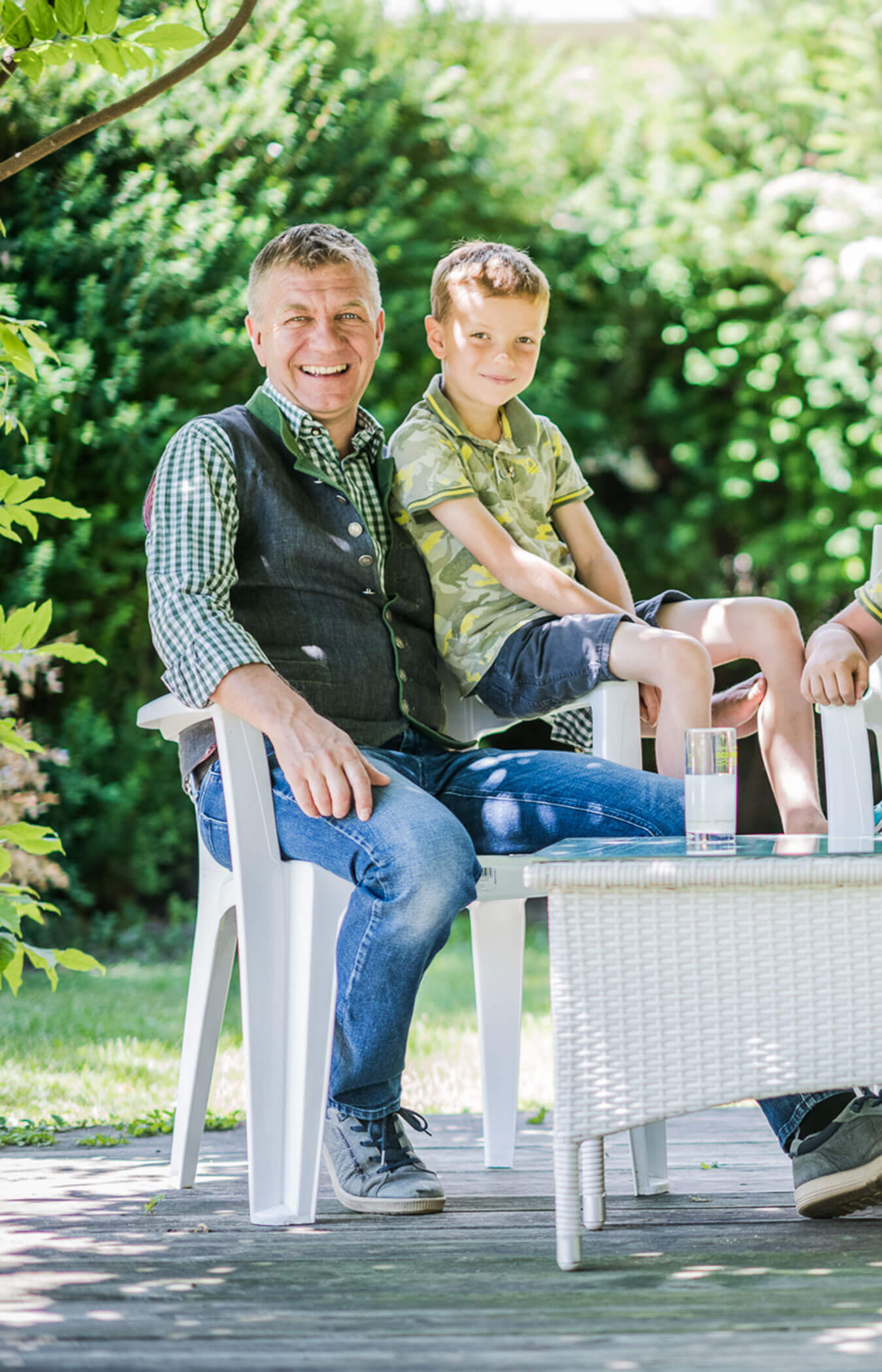 Werner, the host, sits with his son on a chair on the terrace - Wirtshaushotel Alpenrose