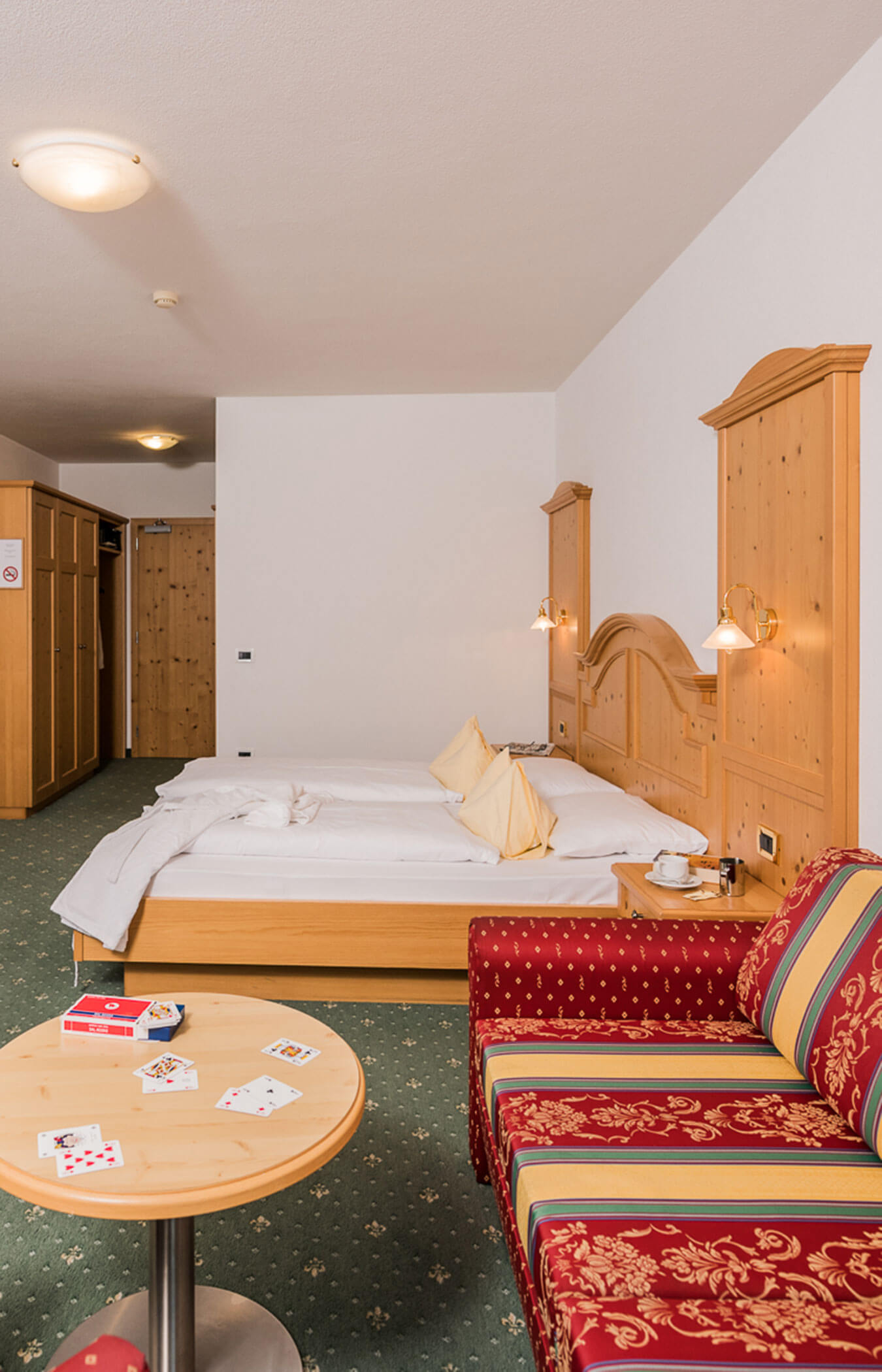 Schlafsofa und Tisch mit Spielkarten im Vordergrund, Doppelbett im Hintergrund - Wirtshaushotel Alpenrose