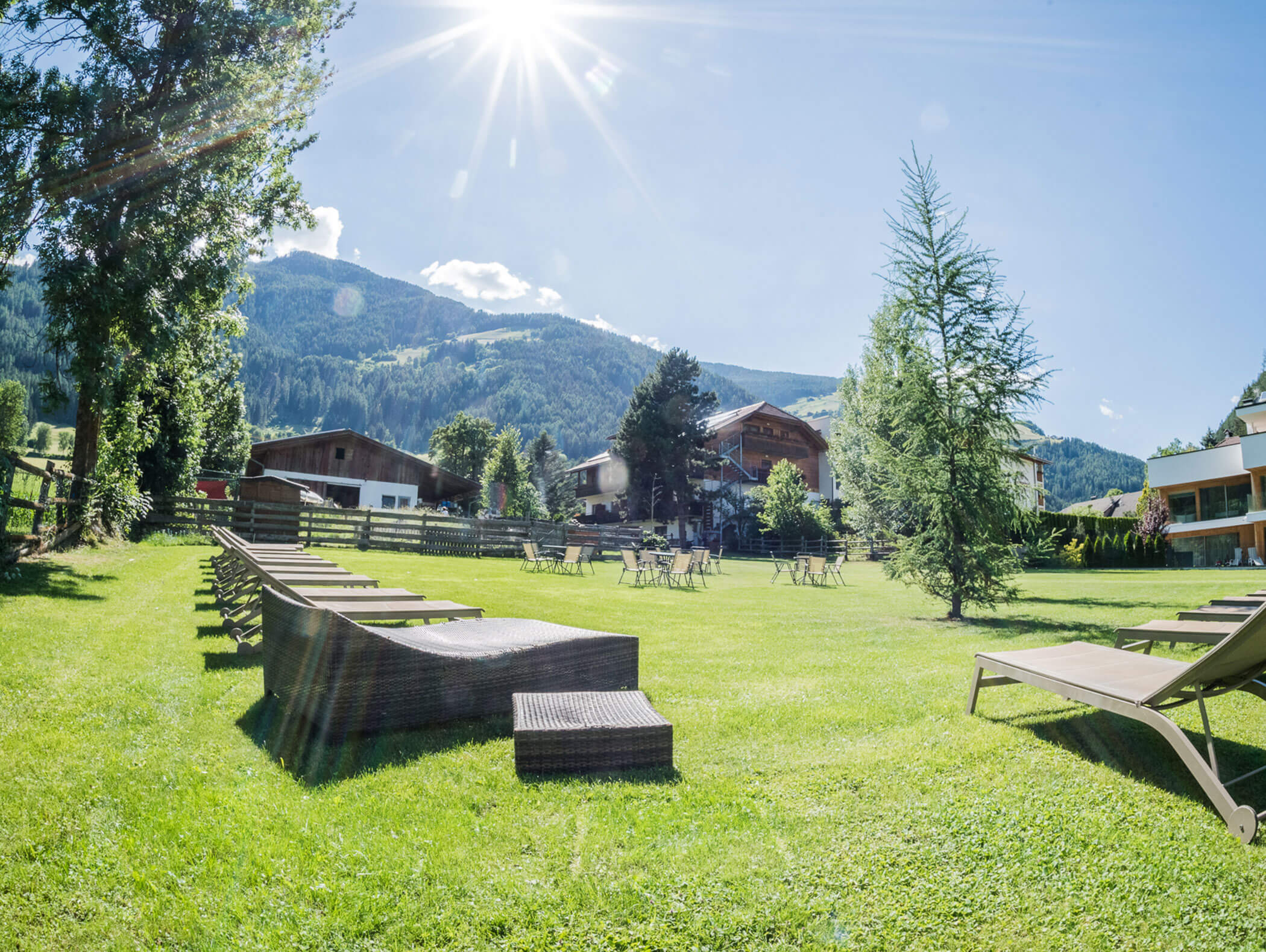 Sun loungers in the garden with trees and farm in the background - Wirtshaushotel Alpenrose