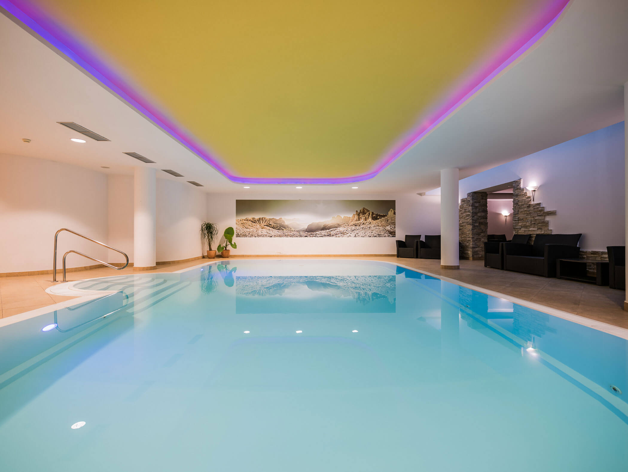 Pool with purple ceiling lighting and seating on the right - Wirtshaushotel Alpenrose