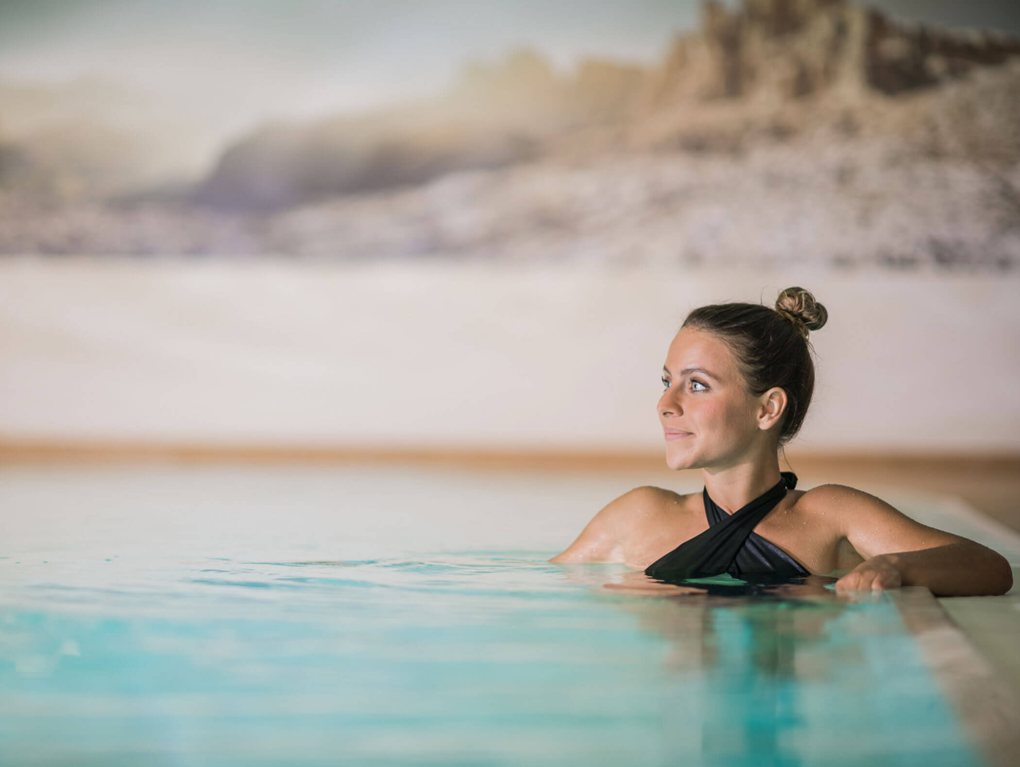Woman stands in the pool and looks into the distance - Wirtshaushotel Alpenrose