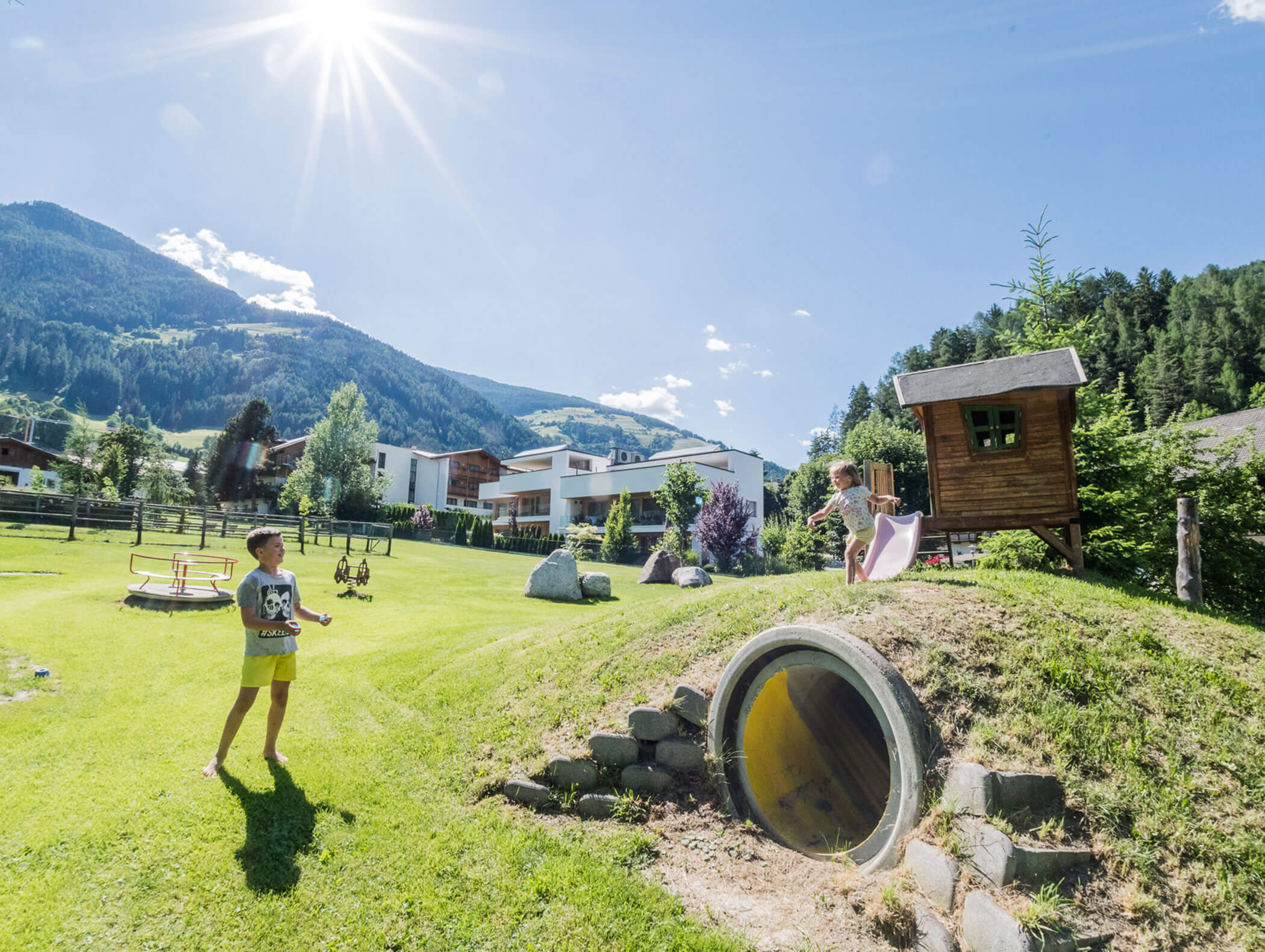 Children in the hotel playground with houses and mountains in the background - Wirtshaushotel Alpenrose