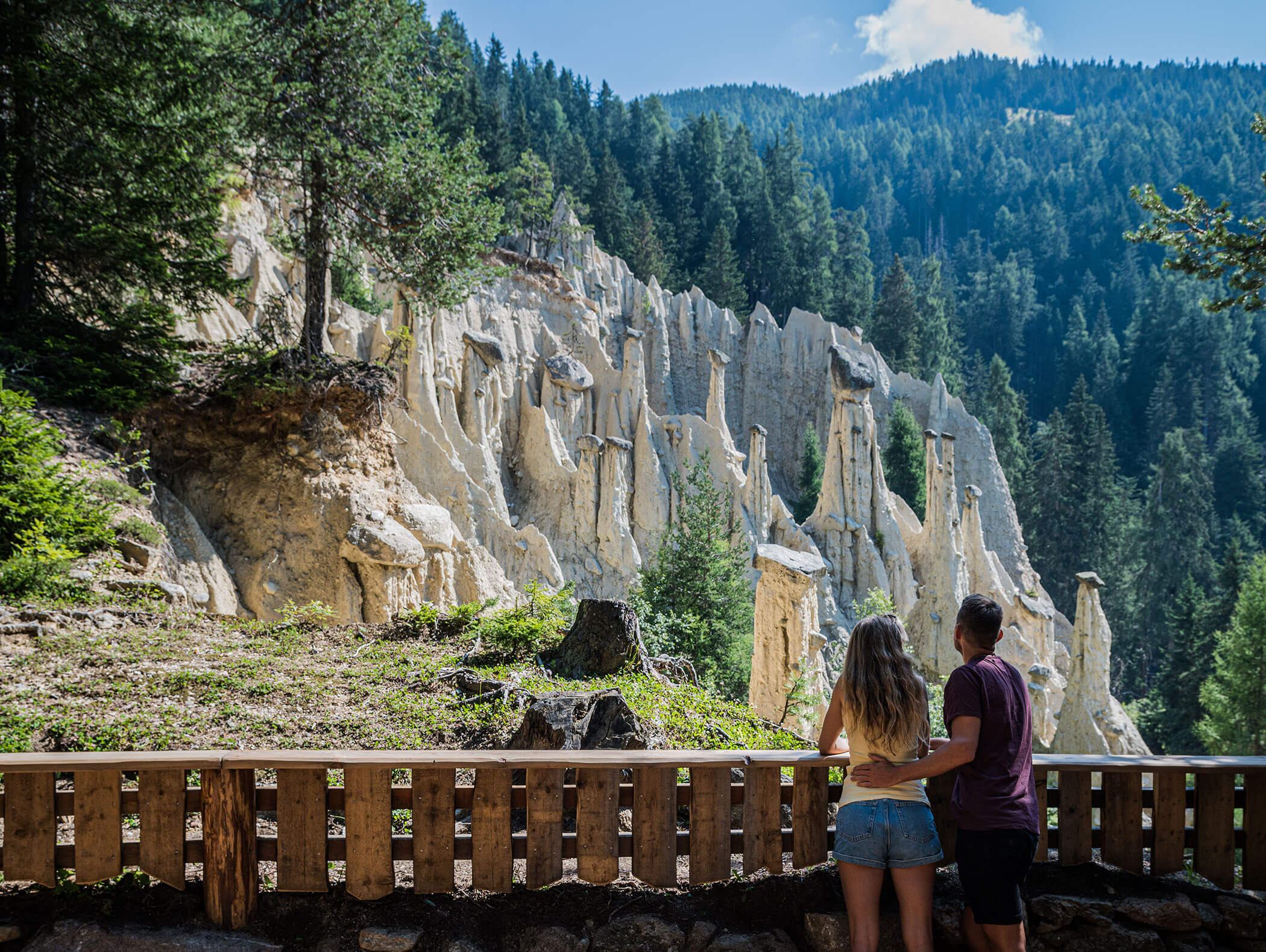 A couple stands in front of a fence and looks at the earth pyramids of Perca - Wirtshaushotel Alpenrose