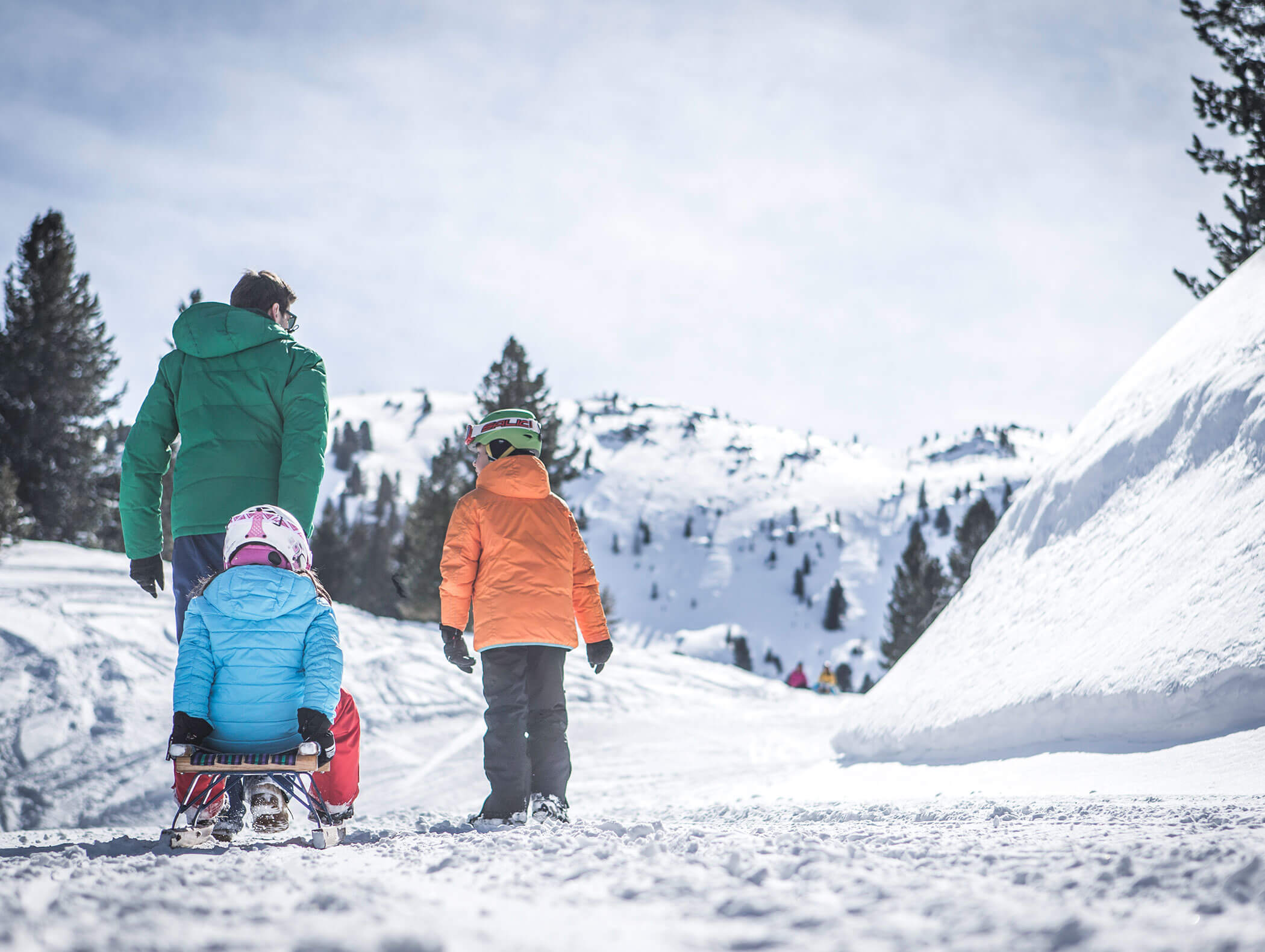Man with two children on the toboggan run with mountains and trees in the background - Wirtshaushotel Alpenrose