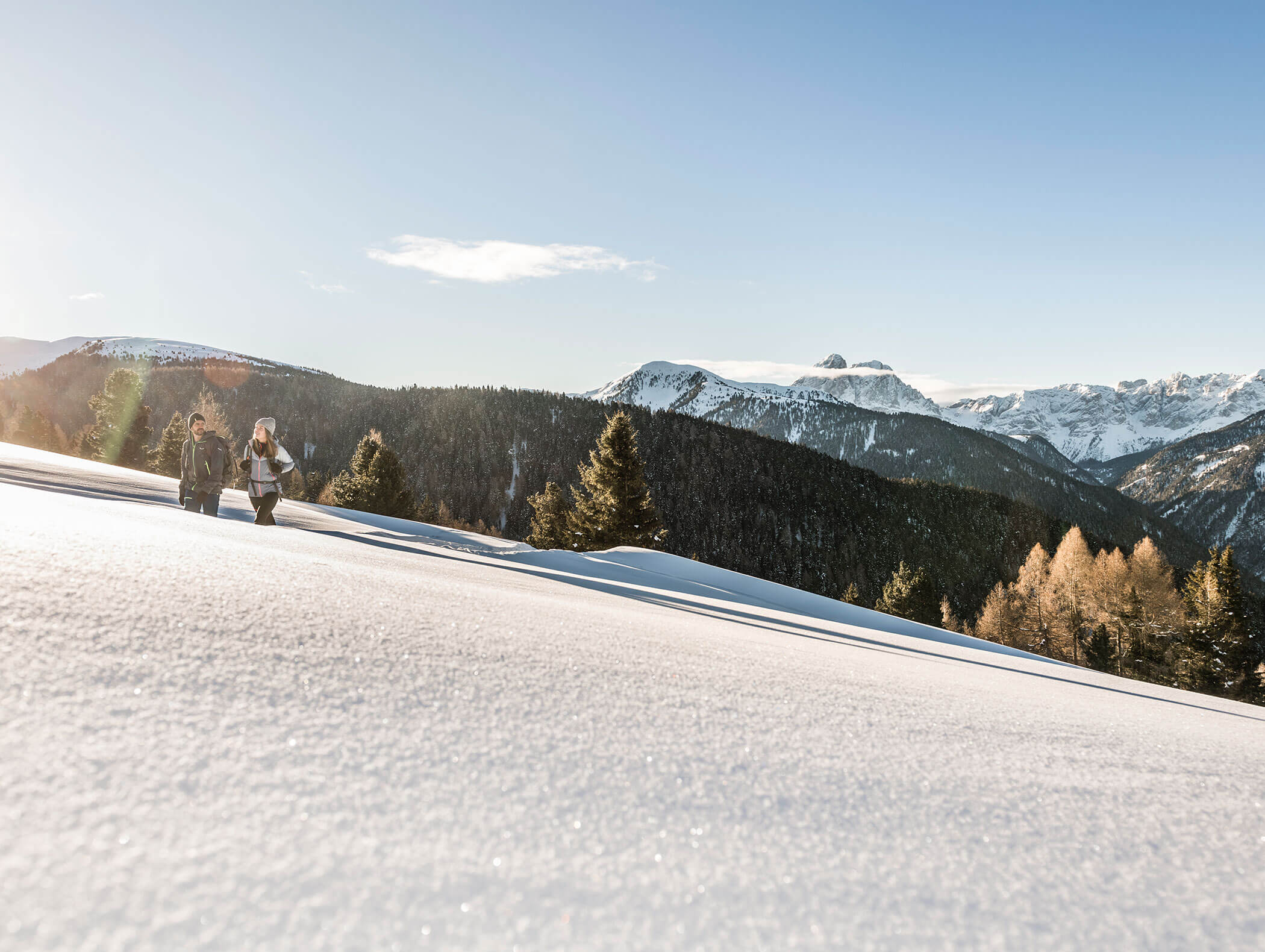 Two hikers in winter with fresh snow in the foreground and forests and mountains in the background - Wirtshaushotel Alpenrose